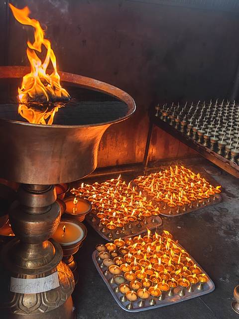 Hundreds of butter lamps burn brightly beside a large bronze urn in a dimly lit Nepalese shrine.