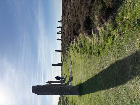 Ancient standing stones of a stone circle on open moorland with two visitors walking beside them under a blue sky.