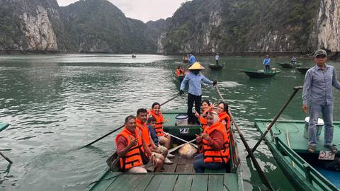 Tourists in orange life vests sit in wooden rowing boats amid limestone karsts of Ha Long Bay.