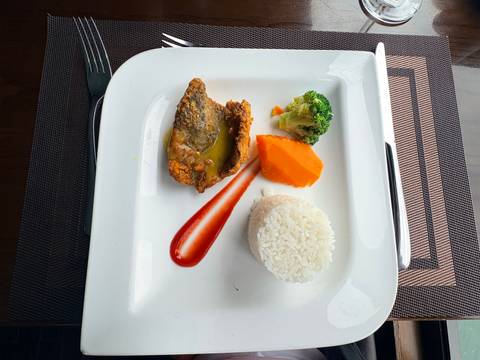 Minimalist presentation of fried fish, vegetables and rice on a square white plate.