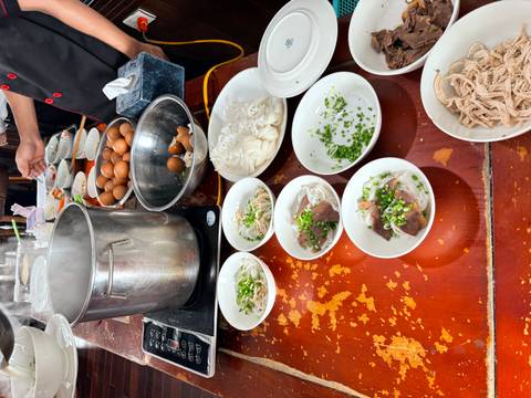 Steaming pot and bowls of noodles, herbs and meat laid out for a pho cooking demonstration.