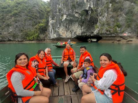 Smiling group wearing life jackets in a small boat near a karst cave entrance in Ha Long Bay.