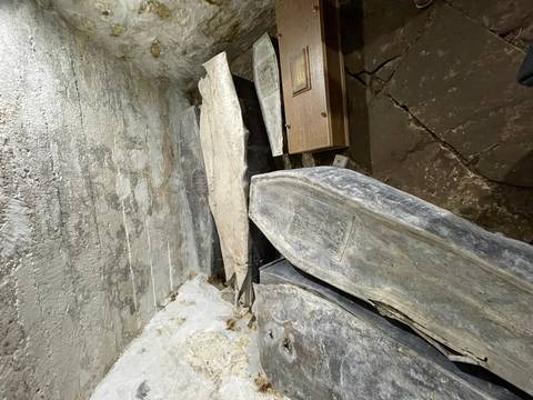 Stone crypt with aged lead coffins and cracked flagstone floor lit by a harsh flashlight.