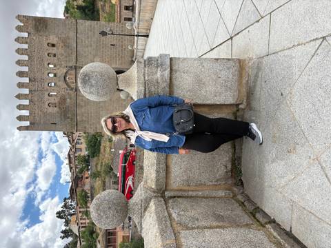 Visitor leans against a granite balustrade on a medieval stone bridge with fortress walls behind.