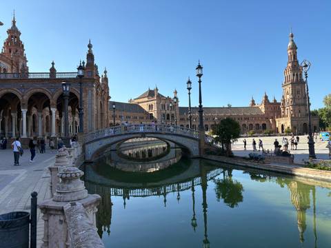 Elegant tiled bridge and soaring towers of Plaza de España reflect in the tranquil canal.