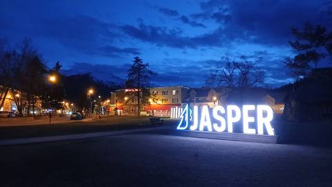 Illuminated JASPER sign glows against a deep blue twilight sky with town lights and mountain silhouettes.