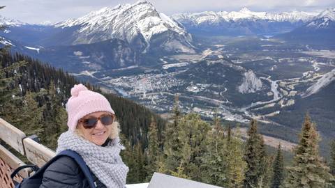 Traveller bundled in winter gear enjoys a panoramic mountain view over Banff townsite from a lookout.