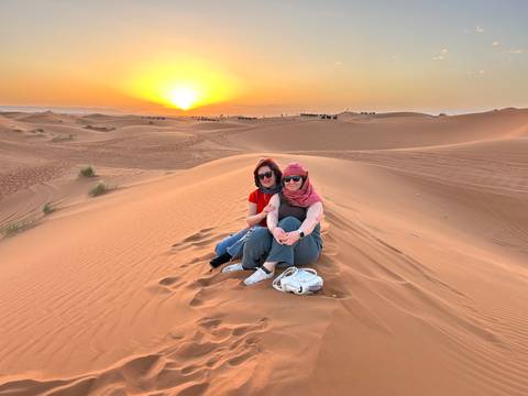 Friends seated on a sand dune enjoy a glowing desert sunset with sweeping vistas.