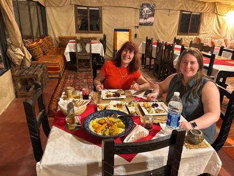 Two travelers dine on traditional Moroccan dishes at a richly decorated camp restaurant.