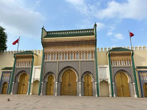Intricate golden gates and green-tiled towers of the Royal Palace in Fes against a blue sky.