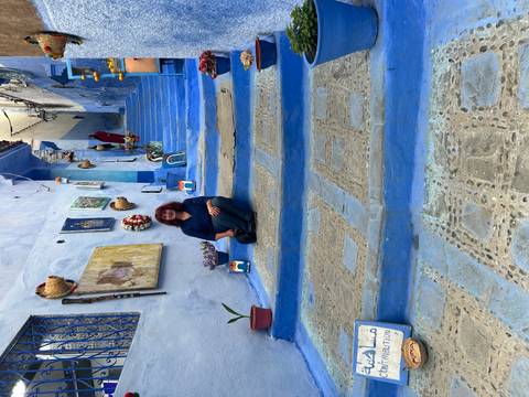 Visitor seated on iconic blue steps adorned with local art in Chefchaouen.