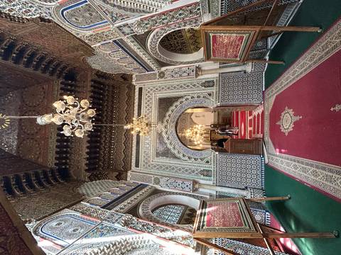 Lavishly decorated interior of a historic mosque or madrasa with detailed zellij and chandeliers.