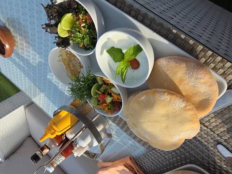 Outdoor table set with pita bread, mezze dishes, fresh herbs and condiments in bright sunlight
