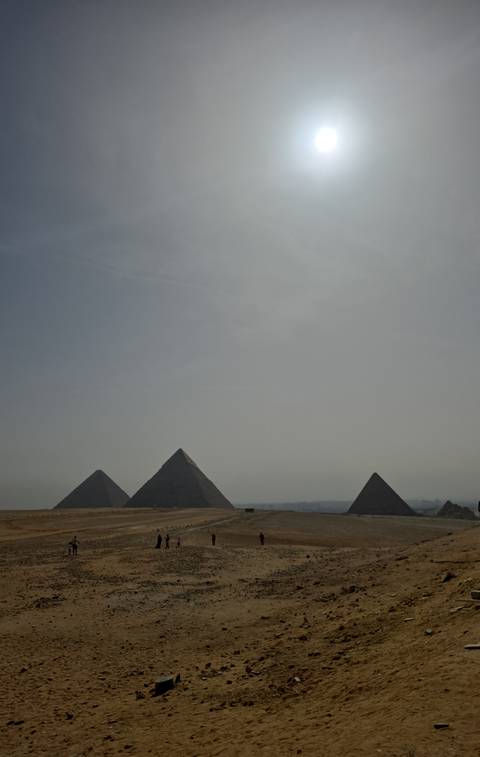 Distant silhouette of three pyramids under a hazy, overexposed sky