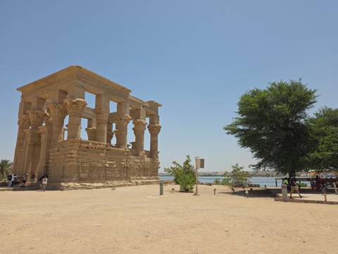 Sand-colored Temple of Philae with ornate columns sits beside the Nile under a clear sky