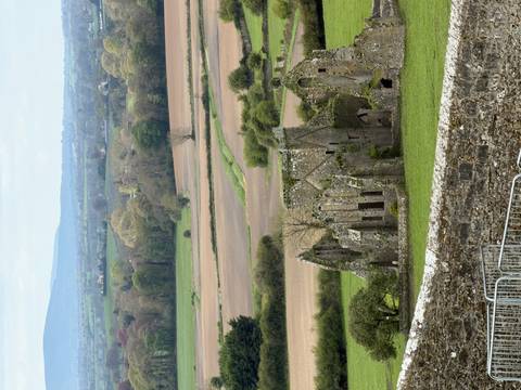 Sweeping rural Irish landscape with ruins of medieval abbey amid patchwork fields.