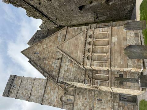 Stone church side wall with Romanesque arches and gravestones in foreground.