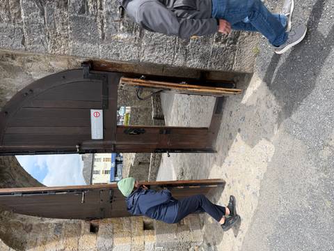 Visitors duck through a narrow wooden castle gate with ‘Mind the Step’ sign.