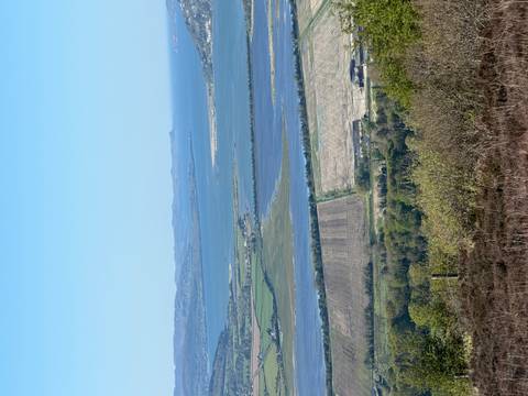 Panoramic view over patchwork farmland, wetlands and distant coastline under a clear blue sky.