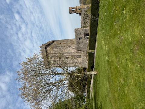 A tall medieval stone tower rising above manicured lawns and hedges beneath a partly cloudy sky.