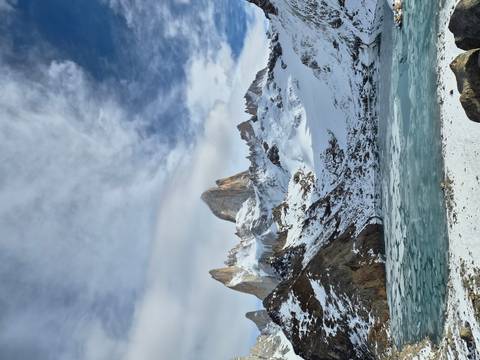 Snow-clad Mount Fitz Roy rises dramatically above a frozen turquoise lagoon under patchy clouds.