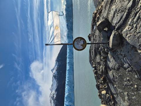 An Argentine flag flutters on a lookout over the vast face of Perito Moreno Glacier and turquoise waters.