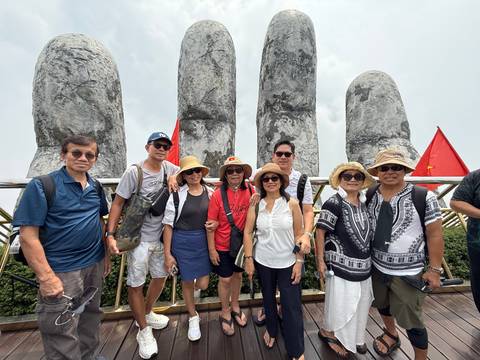 A tour group poses in front of the massive stone hands of Vietnam’s Golden Bridge on a cloudy day.
