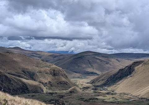 Rolling Andean highlands under dramatic clouds with a remote valley floor and rugged ridges.