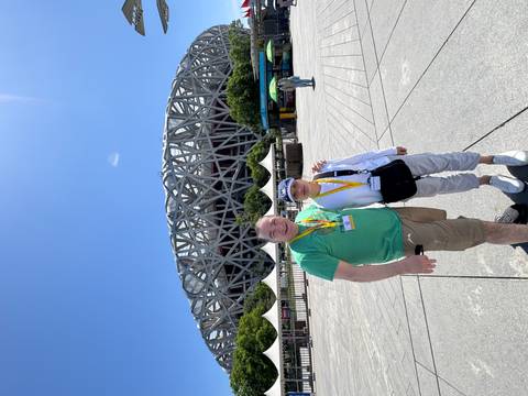 Smiling couple posing in front of Beijing’s Bird’s Nest Olympic Stadium under a bright blue sky.