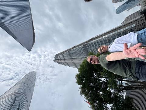 Up-angle shot of a couple reaching toward the camera with Shanghai’s soaring skyscrapers and dramatic clouds above.