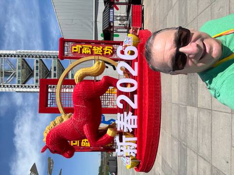 Selfie of a man in front of a bright red horse statue and large 2026 New Year display.