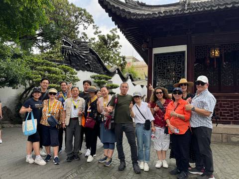 Group tour photo in a classical Chinese garden with a serpentine dragon wall and manicured greenery.