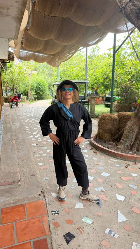 Young traveller in a black jumpsuit and sunhat confidently poses on a garden pathway.