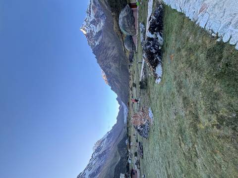 Broad alpine valley ringed by snow-covered Andean peaks with a lone trekker near eco-domes at dawn