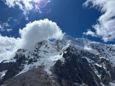 Snow-clad Andean peaks pierce the sky with a dramatic cloud plume lit by bright sun