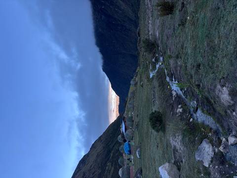 Remote campsite domes beneath misty ridges and a blue twilight sky with a trickling stream in foreground