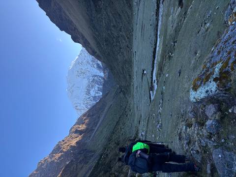 Early-morning trekker approaches a steep snow-covered Andean pass through a glacial valley