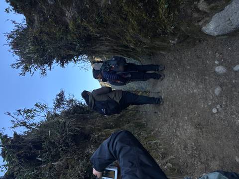 Two trekkers pause between high earthen walls on a narrow mountain trail in cool morning light