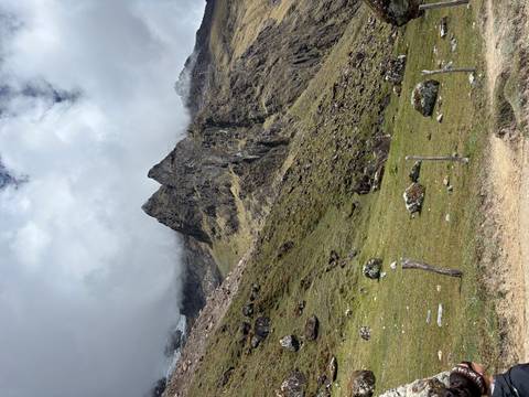 Jagged rocky peaks rise through swirling clouds above grassy alpine slopes scattered with boulders
