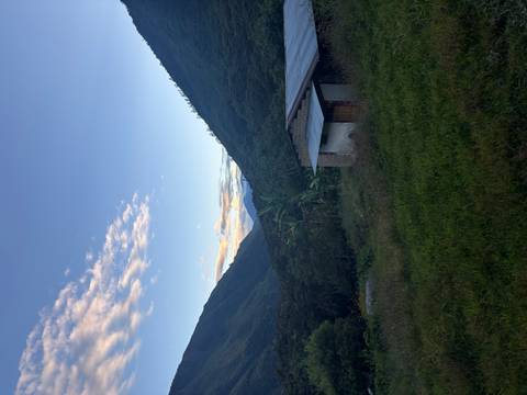 Twilight view down a lush green valley toward distant snow-capped peaks with a rustic hut in foreground