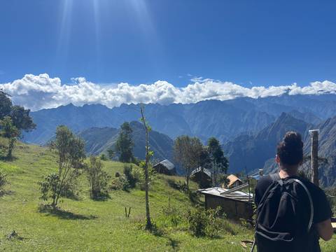 Hiker looks over dramatic layers of Andean ridges under billowing clouds from a grassy hillside