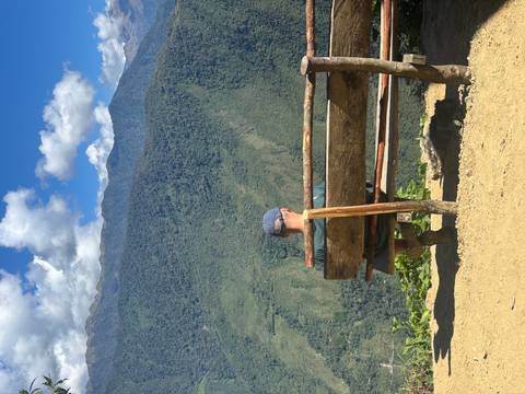 Man sits on a rustic bench at a scenic overlook with sweeping green valleys below and a dog resting underneath