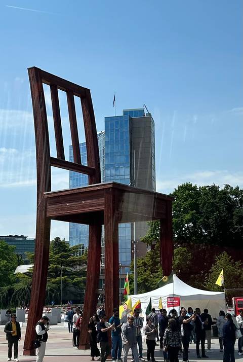 The giant wooden 'Broken Chair' sculpture stands tall before a modern glass office tower on a bright day.