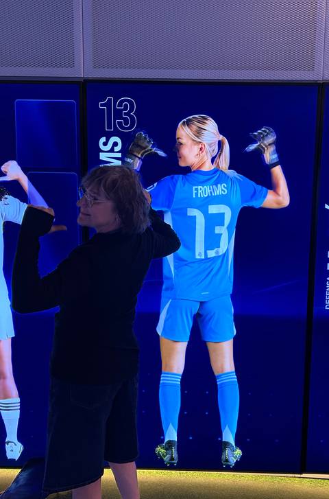 A visitor poses playfully in front of an illuminated sports exhibit featuring a football player's jersey.