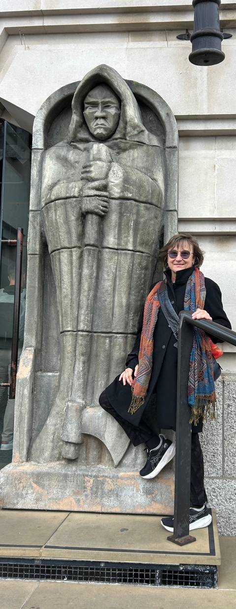 A traveller in a colorful scarf leans on a railing beside an ornate stone column.