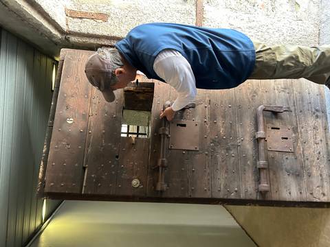 A man inspects an old wooden prison door display inside a historic building.
