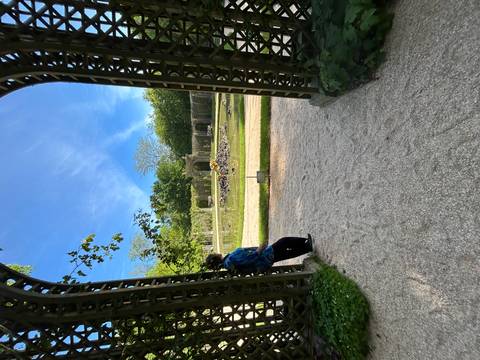 A woman gazes across a tranquil fountain pond framed by lattice arches and lush greenery.