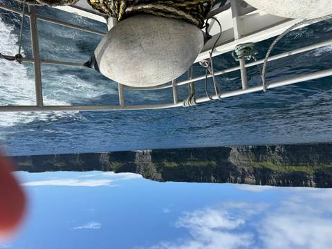 View of towering sea cliffs from the deck of a boat with a finger slightly obscuring the lens.