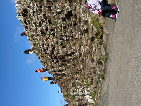 Visitors explore the hexagonal basalt steps of the Giant's Causeway slope on a sunny day.