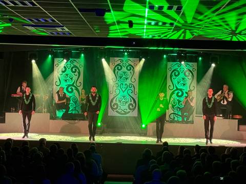 An energetic Irish dance performance unfolds on stage under vivid green lighting.